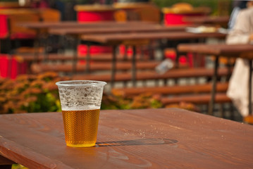 Beer in a plastic glass close-up. Alcoholic beverage at the festival. Glass on an old wooden table with scratches and crumbs of bread.