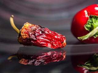 Dry and fresh red sweet peppers on glossy surface with reflection