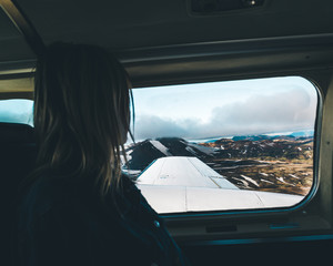The  girl sitting in plane and looking outside on the majestic landmannalaugar mountains on iceland