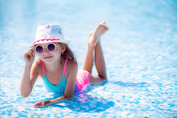 Little girl in Sunglasses and hat with unicorn in outdoor swimming pool of luxury resort on summer...
