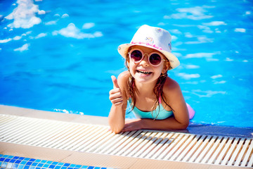 Happy girl in Sunglasses and hat with unicorn show thumb up in outdoor swimming pool of luxury...