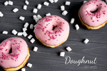 Three pink doughnut on a dark wooden background with marshmallows. Donuts with pink glaze closeup. No diet