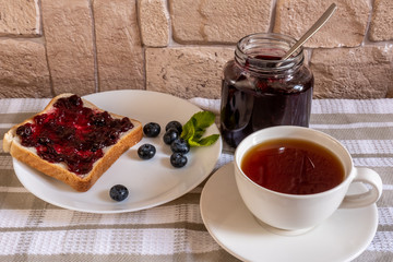 The toast with blueberry jam and a can with huckleberry jam on a light background
