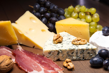 Assorted cheeses, nuts, grapes, fruits, smoked meat and a glass of wine on a serving table. Dark and Moody style.