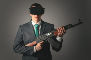 Businessman with a assault rifle in hand and in virtual reality glasses isolated on gray background.