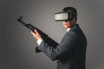 Businessman with a assault rifle in hand and in virtual reality glasses isolated on gray background.