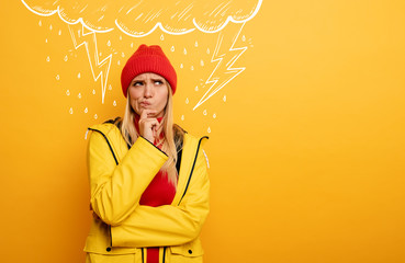 Girl thinks about negative things. Cloud, rain and lightning above her. Confused and pensive expression. Yellow background