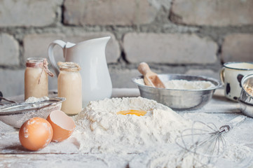 Egg, flour, milk and bowl opn wooden table. Ingredients for dough