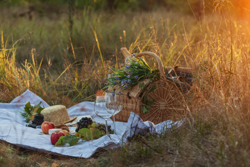 Picnic basket with grapes, apples, cheese, croissants, wine in the forest at sunset. Picnic for two, concept of meeting