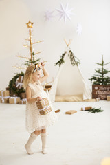 A portrait of a little girl near the wigwam and Christmas tree unpacking Christmas gifts on a white background