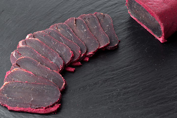 Cured meat on a slate board. Close-up of basturma sliced into pieces.