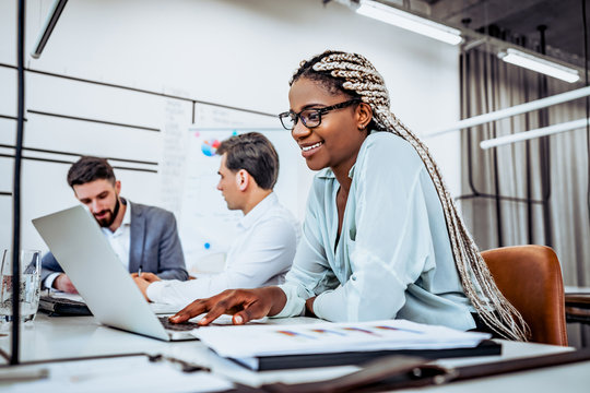 I love my job! A young American business woman works in an office with colleagues in the background.