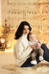 A beautiful young mother with a baby in a Christmas decorated room near the Christmas tree on a background of lights and music