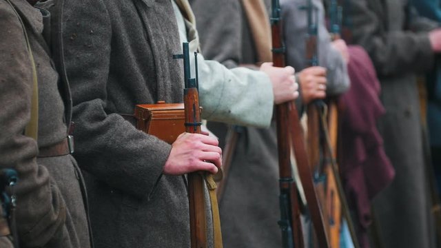 Men soldiers in coats standing in the row holding guns - clapping with frozen hands