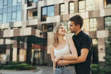 Stylish happy couple hugging on urban background, looking at each other and smiling. Street portrait of a loving couple on a walk. Love story concept.