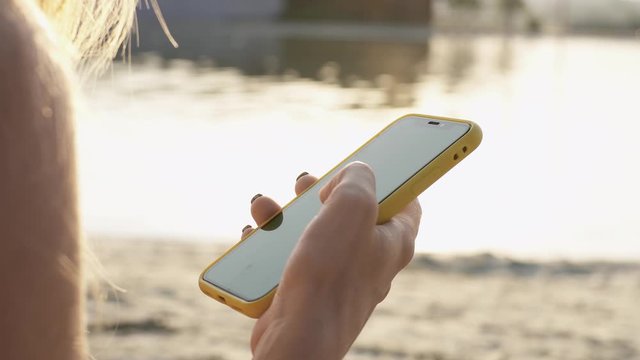 At sunlight young woman hands use smartphone vertical green screen background sand beach lake summer technology cellphone chroma key working communication device display sun relaxation slow motion