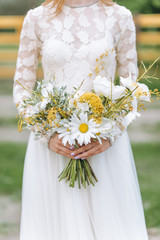 A beautiful young bride with a bouquet of daisies in a field