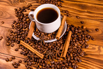 Cup of hot coffee, star anise, cinnamon sticks and scattered coffee beans on wooden table