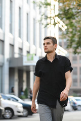 Handsome man in casual casual clothes strolling down the street in the modern city and looking away, wearing a dark shirt.Street style portrait. Fashionable guy walking down the street,photo in motion