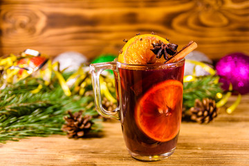 Cup of mulled wine with cinnamon, christmas decorations and fir tree branches on wooden table