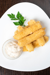 Cheese sticks breaded, with sauce and herbs, on a platter.
