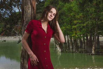 a beautiful, young brown-haired woman in a red dress on the background of a morning lake with cypresses, a girl with a slender figure posing against nature