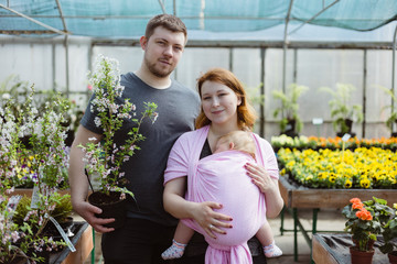 Young family shopping for shrubs and plants for their garden in a local retailer's greenhouse nursery.