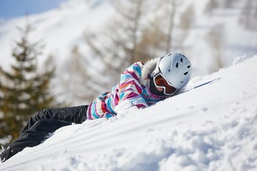 Skier lying in the deep snow playing wearing helmet and goggles on the snowy slope