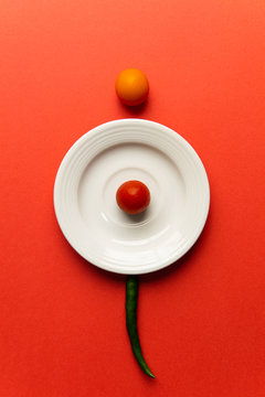 two small cherry tomatoes and one green chilli pepper, white plate and vivid background