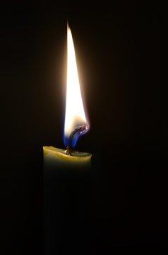 A green lit candle in the dark, the flame illuminating only toe top of the candle, the tip of the wick glowing.