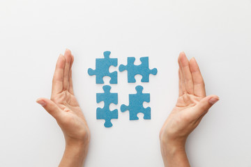 cropped view of woman hands near pieces of blue jigsaw puzzle on white background