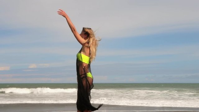 Beautiful young woman in neon bikini and light black summer dress. Fitness healthy active living. Sport and travel. Weight loss and body image concept. Girl with perfect fit body on tropical beach.