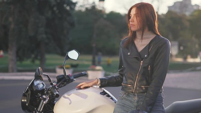 beautiful young red-haired woman motorcyclist in a leather jacket on bike