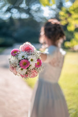 Silhouette of bride in white lace wedding dress in background that holds wedding bouquet flower composed of white roses, pink gerberas and ornamental flowers.