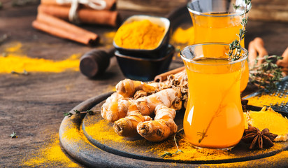 Healthy vegan turmeric golden tea with honey in glass cup on wooden tray. Herbal healing spicy tea