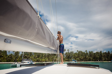 Young man preparing mainsail of catamaran 