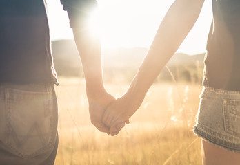 Couple holding hands walking together in sunset nature setting. 