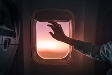 Female's hand opening airplane window at sunset. People traveling by airplane, transportation, vacation concept.