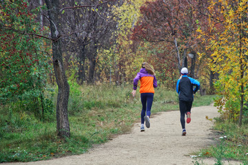 Young girls are training on the run in the autumn park alley. Activity and sport. Unrecognizable