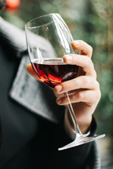 man holding wine glass. A glass of red wine holding by man wearing spring coat, smelling red wine before tasting and drinking it. Low key portrait.