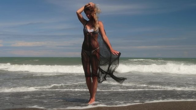 Beautiful young woman in white bikini and light black summer dress. Fitness healthy active living. Sport and travel. Weight loss and body image concept. Girl with perfect fit body on tropical beach.