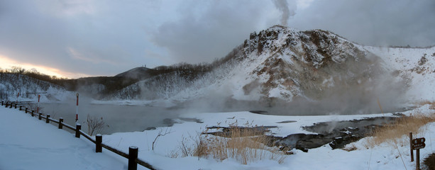 Hiking trail near Volcanic lake, steam rising from thermal water, volcano with rising smoke, Jigokudani hell valley winter volcanic landscape panorama, Noboribetsu famous place