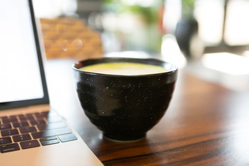 Golden milk matcha latte with turmeric, on coffee shop table next to laptop, copy space