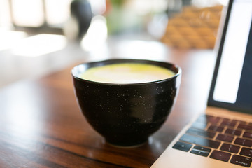 Golden milk matcha latte with turmeric, on coffee shop table next to laptop, copy space