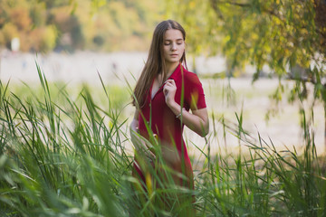 a beautiful, young brown-haired woman in a red dress on the background of a morning lake with cypresses, a girl with a slender figure posing against nature