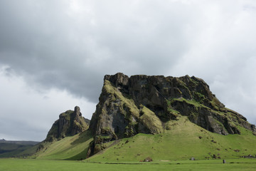 A horizontal shot of two large jagged outcroppings jut up from a moss covered plain.