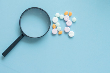 Magnifying glass with pills on blue background. pharmaceutical inspection identifies pills....