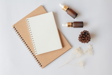 Flat lay of organic aromatherapy oils or skincare products for mock up in minimal style. Dropper glass bottle with notebook, pine cone and dry flower on white background.