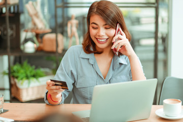 Asian woman using mobile phone with credit card and laptop computer for shopping online payment in coffee shop cafe with freinds