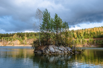 Autumn landscape. A stone island with trees in the middle of a lake surrounded by forest. Russia. Siberia.